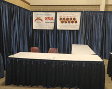 Load image into Gallery viewer, Booth; Corner - Two 8ft “L shape&quot; skirted tables w/ white table cloth, back drop, &amp; 3 chairs.
