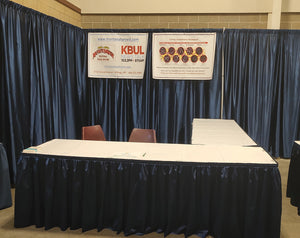 Booth; Corner - Two 8ft “L shape" skirted tables w/ white table cloth, back drop, & 3 chairs.