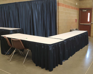 Booth; Corner - Two 8ft “L shape" skirted tables w/ white table cloth, back drop, & 3 chairs.